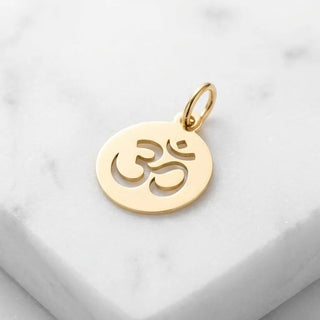 Gold pendant with Om symbol on a white marble surface