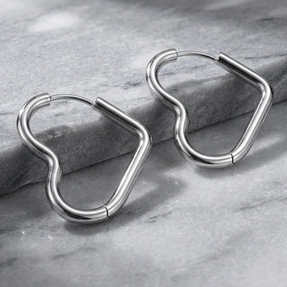 Pair of heart shaped silver hoop earrings on a gray stone surface