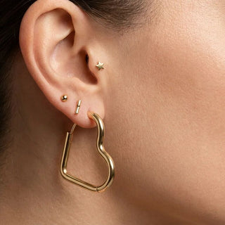 Close-up of an ear with gold hoop earrings and small studs.