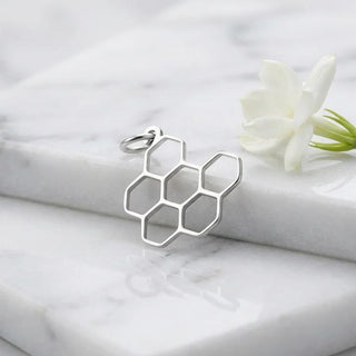 Silver honeycomb pendant on a marble surface with a white flower
