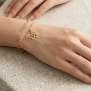 Gold honeycomb bracelet on a hand against a neutral background