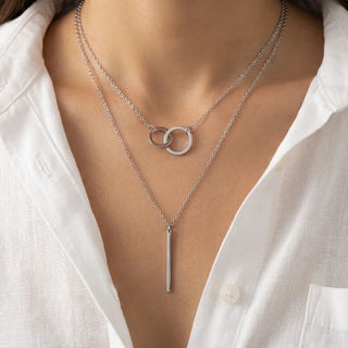 Silver necklace with interlocking rings and a vertical bar on a white shirt background