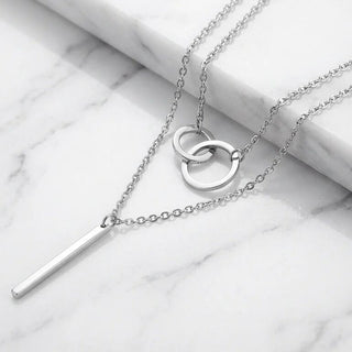 Silver necklace with interlocking rings and a bar pendant on a marble surface