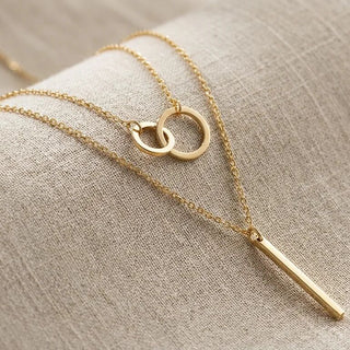 Gold necklace with interlocking rings and a bar pendant on a beige fabric background