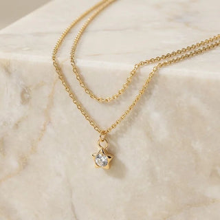 Gold necklace with a star-shaped pendant on a marble surface