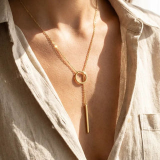 Gold necklace with a pendant worn by a person in a light-colored shirt.