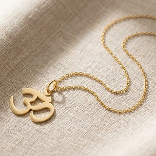 Gold Om symbol necklace on a textured beige fabric background