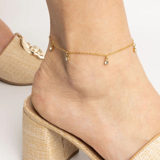 Gold anklet on a foot with a neutral background