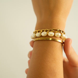 Gold bracelet with pearls on a wrist against a neutral background