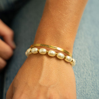 Gold bracelet with pearl beads and 'Enjoy the Journey' message on wrist against denim background