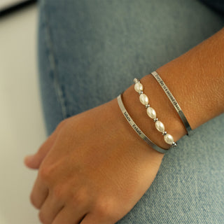 Bracelets with pearls and text on a wrist against a denim background