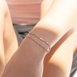 Silver cross bracelet on a person's wrist with a blurred background