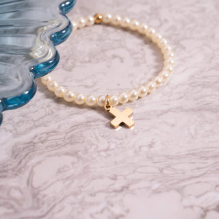 Pearl bracelet with a gold cross charm on a textured surface