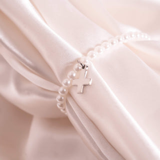 Pearl bracelet with a silver cross on a soft white fabric background