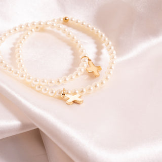Pearl bracelet with gold cross pendants on a soft fabric background