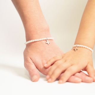 Two hands wearing pearl bracelets with small charms on a light background