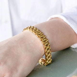 Gold bracelet on a wrist with a neutral background