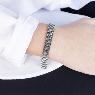 Metallic bracelet on a person's wrist with a white shirt and black pants in the background