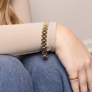 Person wearing a gold and silver bracelet on a light background