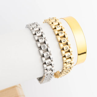 Two bracelets, one silver and one gold, on a light gray background