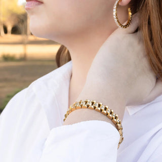 Close-up of a person wearing gold hoop earrings and bracelet with a blurred outdoor background