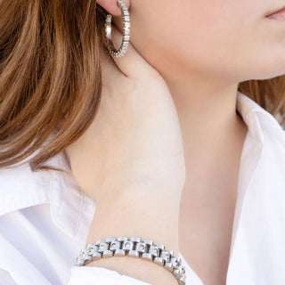 Close-up of a person wearing silver hoop earrings and bracelet.