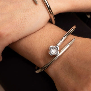 Silver bracelet with a flower charm on a wrist against a dark background