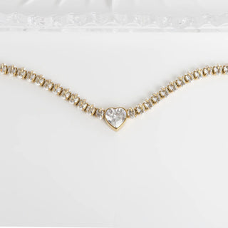 Gold necklace with a heart-shaped diamond pendant on a white background