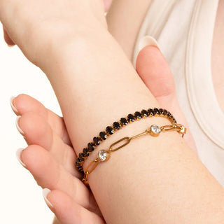 Gold bracelet with dark stones on a wrist against a neutral background