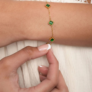 Gold bracelet with green gemstones on a wrist against a white background