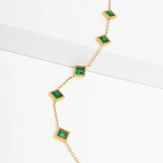 Gold necklace with green gemstones on a white background