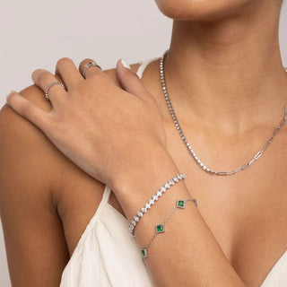 Close-up of a person wearing silver jewelry including a necklace, bracelet, and ring on a neutral background.