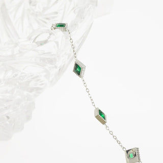 Silver bracelet with green gemstones on a textured white surface