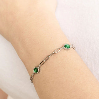 Silver bracelet with green gemstones on a wrist against a white background