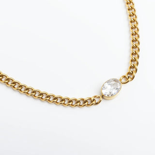 Gold chain necklace with a clear gemstone on a white background