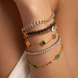Multiple gold and gemstone bracelets on a wrist against a neutral background