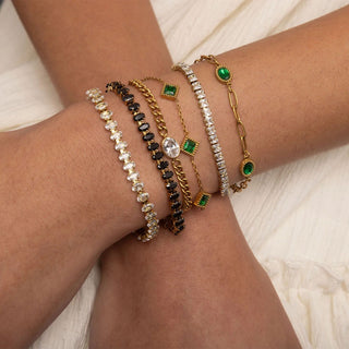 Close-up of a wrist wearing multiple bracelets with green gemstones on a light background