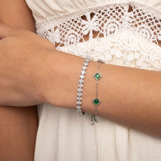 Close-up of a wrist wearing two silver bracelets with green gemstones, against a white lace garment.