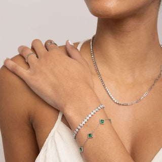 Person wearing silver jewelry including a necklace, bracelet, and ring on a plain background