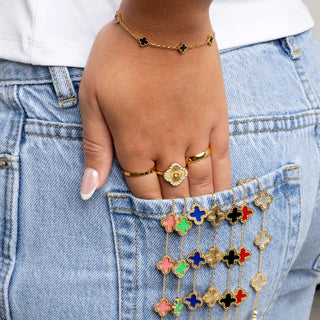 Hand with gold rings and colorful flower-shaped pendants on a denim background