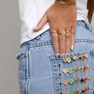 Close-up of a hand with gold rings on a denim pocket with colorful floral charm bracelets.