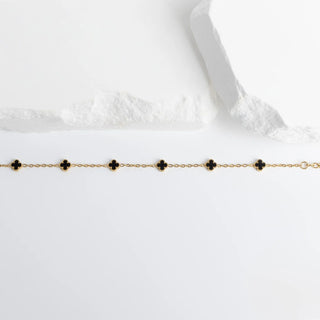 Gold bracelet with black floral-shaped charms on a white background