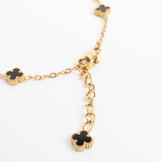 Gold bracelet with black flower-shaped charms on a white background