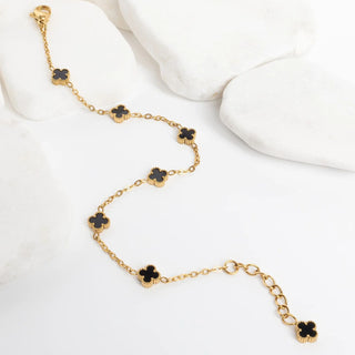 Gold bracelet with black flower-shaped charms on a white surface