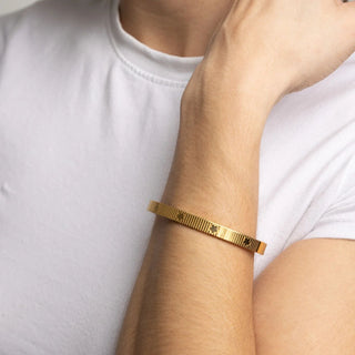 Gold bracelet on a person's wrist against a white background