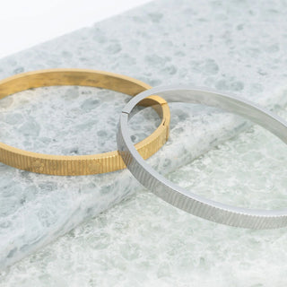 Two metal rings, one gold and one silver, on a marble surface.