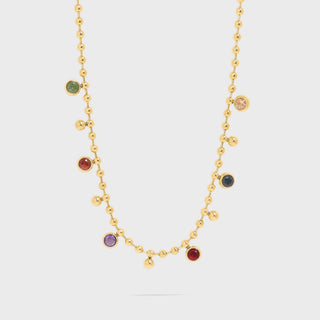 Gold necklace with colorful gemstones on a light gray background