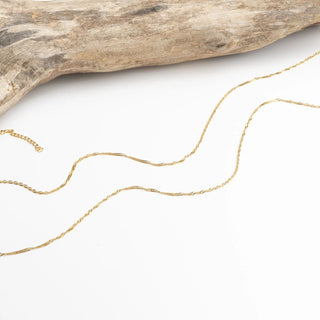 Gold Singapore Belly Chain on a white surface with a piece of driftwood.