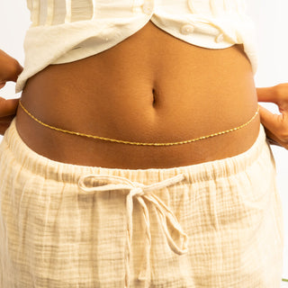 Person wearing a beige top and pants with a thin gold Singapore Belly Chain.