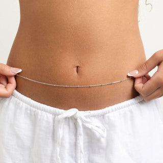 Person wearing white pants with a silver Satellite Belly Chain around the waist on a plain background
